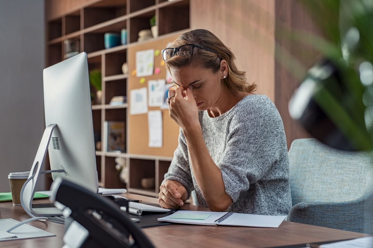 Erschoepfte Frau am Schreibtisch reibt Stirn – typisches Bild fuer Funktionsmodus im Alltag, Thema: Stressabbau mit Coach Berlin