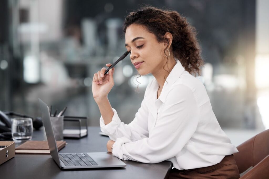 Nachdenkliche Frau vor Laptop mit Stift – Symbol für innere Reflexion im Alltag, Thema: Selbstcheck mit Coach Berlin