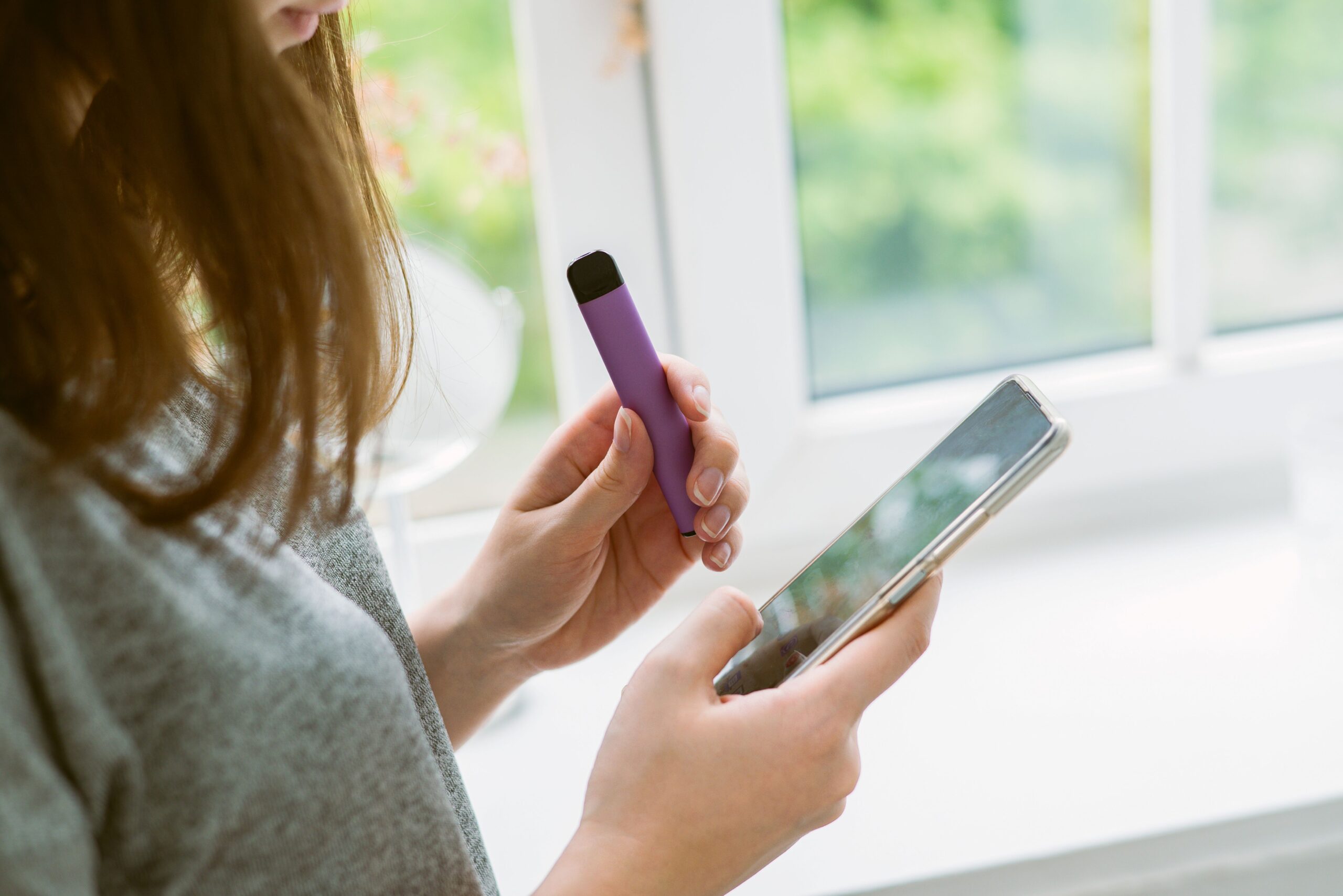 Frau hält modernes Vape-Gerät und Smartphone