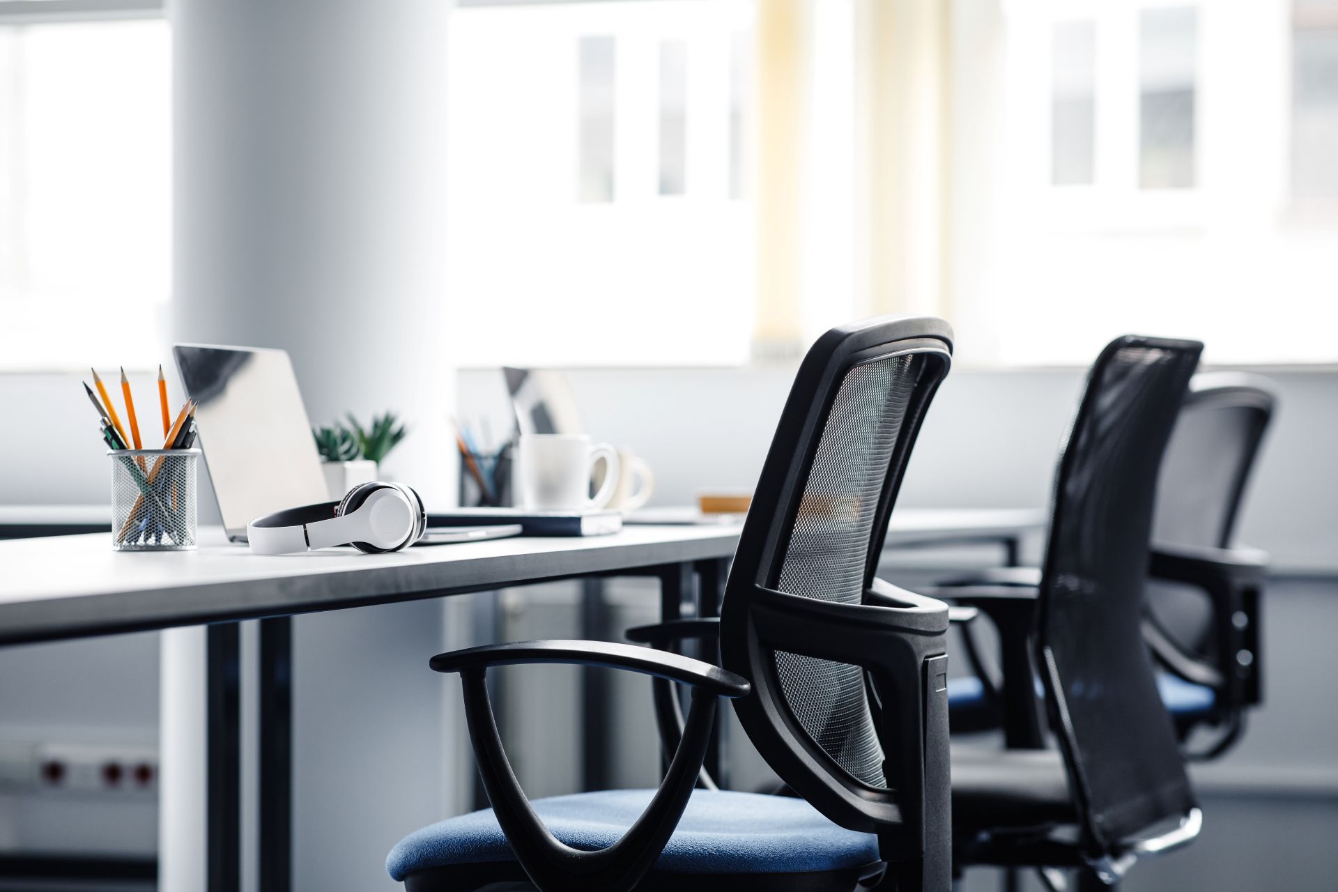 Ergonomische Bürostühle an hellem Schreibtisch mit Laptop